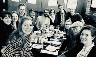 Group of smiling people gathered around a long dining table in a restaurant, posing for a meal photo.