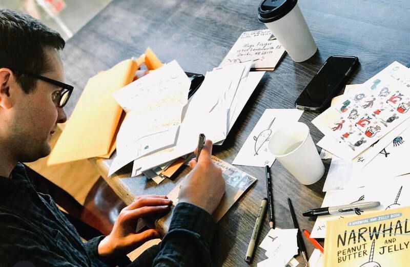 Person sketching at a cluttered desk with papers, coffee cup, and design notes