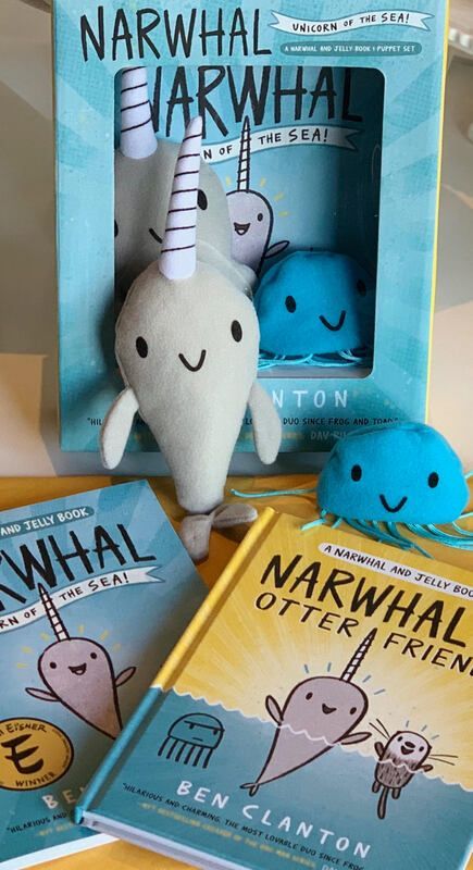 Narwhal plush and books displayed together, with a smiling blue plush and colorful covers.