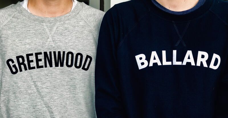 Two people in gray and navy sweatshirts with “GREENWOOD” and “BALLARD” printed across the chest.