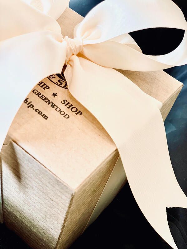 Gift box wrapped in cream satin ribbon with a tag on a pale wooden surface