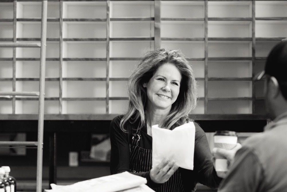Woman smiling and holding papers in a meeting room with shelves behind her