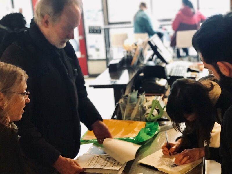 People at a table writing on forms during a community event