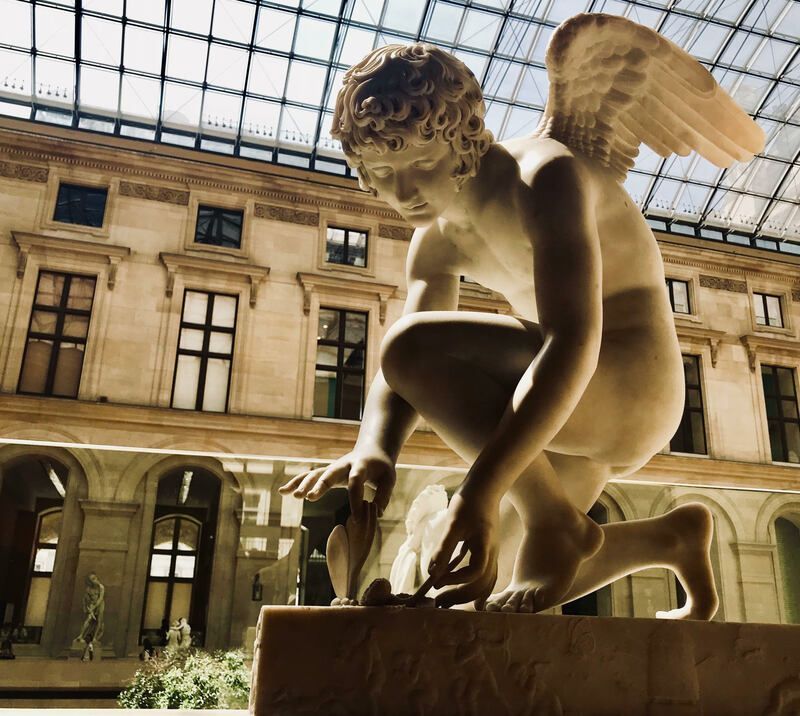Golden winged statue in a sunlit courtyard beneath a glass سقف