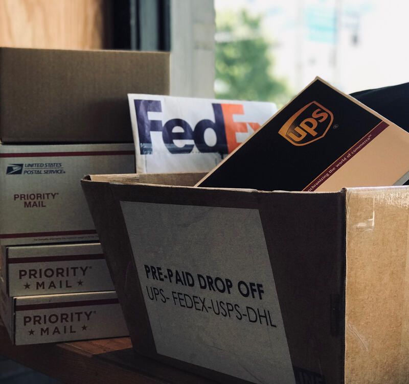FedEx and UPS packages in a USPS drop-off box beside Priority Mail boxes