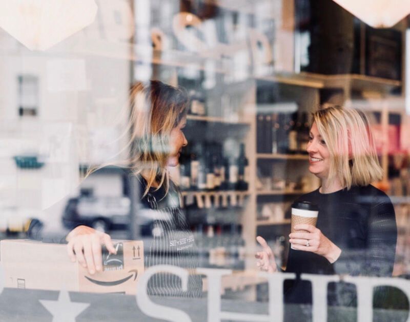 Two people chatting in a café, one holding a coffee cup by the window.