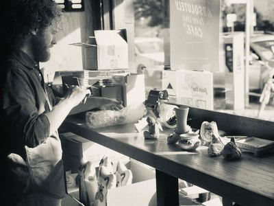 Person serving food at a café counter with pastries and cups by the window