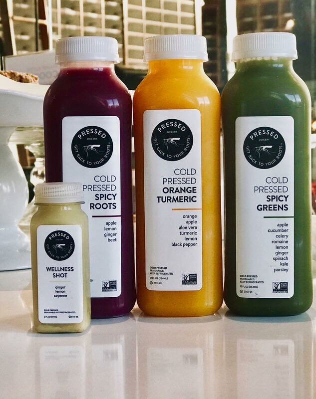 Four cold-pressed juice bottles in red, orange, green, and white on a countertop.