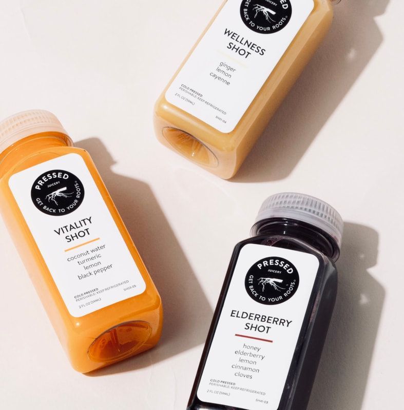 Three wellness shot bottles in orange, beige, and dark purple on a light background