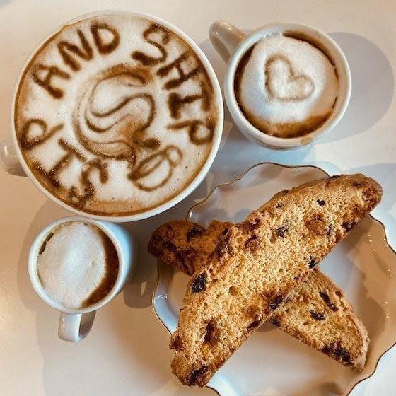 Coffee cups and biscotti arranged on a tray, with latte art reading “AND SHE.”
