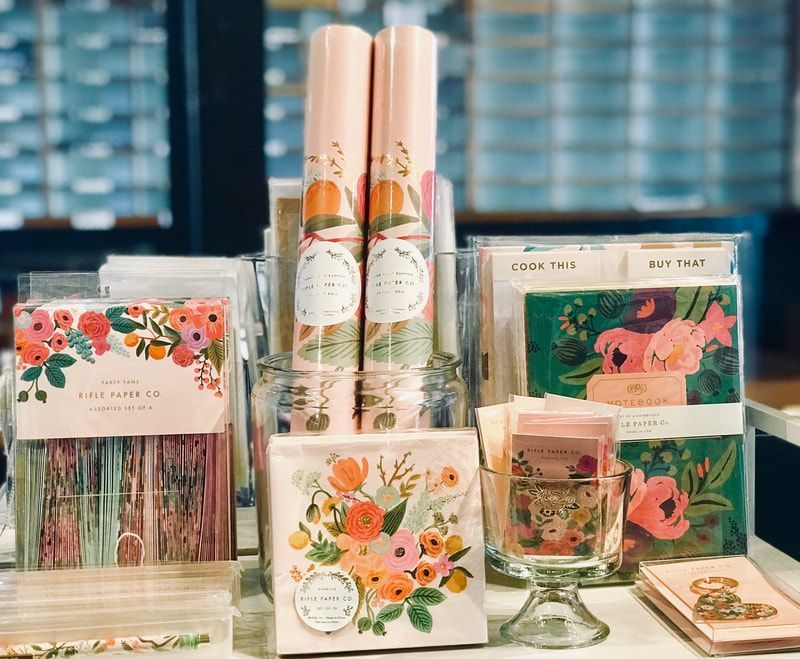 Pastel floral stationery and gift set display with notebooks, pens, candles, and mugs