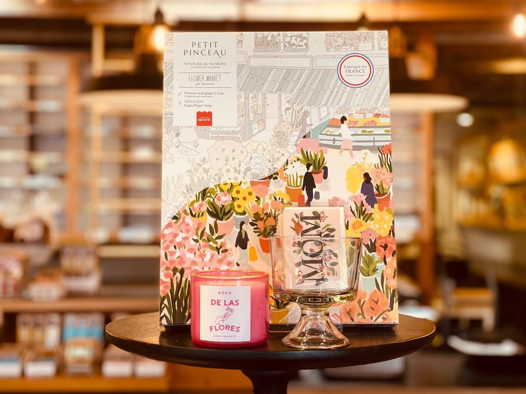 Candles and a floral gift box on a tray with a map card, in a warm bakery or café setting