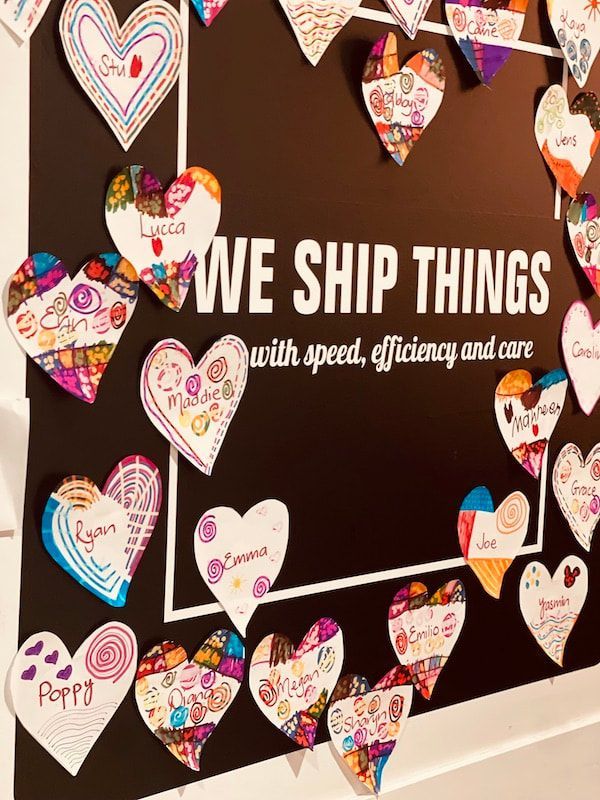 Heart-shaped Valentine notes cover a wall sign reading “WE SHIP THINGS with speed, efficiency and care”