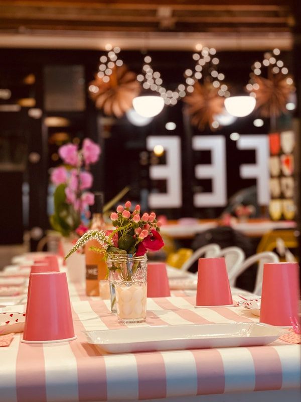 Café table with pink checkered cloth, flowers, and pink cups in a softly lit restaurant interior