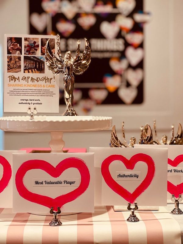 Pink heart-shaped cards with names on a striped table, with a small trophy and display stand behind them