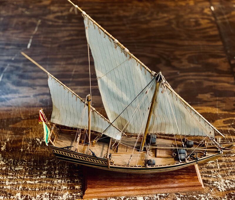 Model sailboat with white sails on a wooden surface