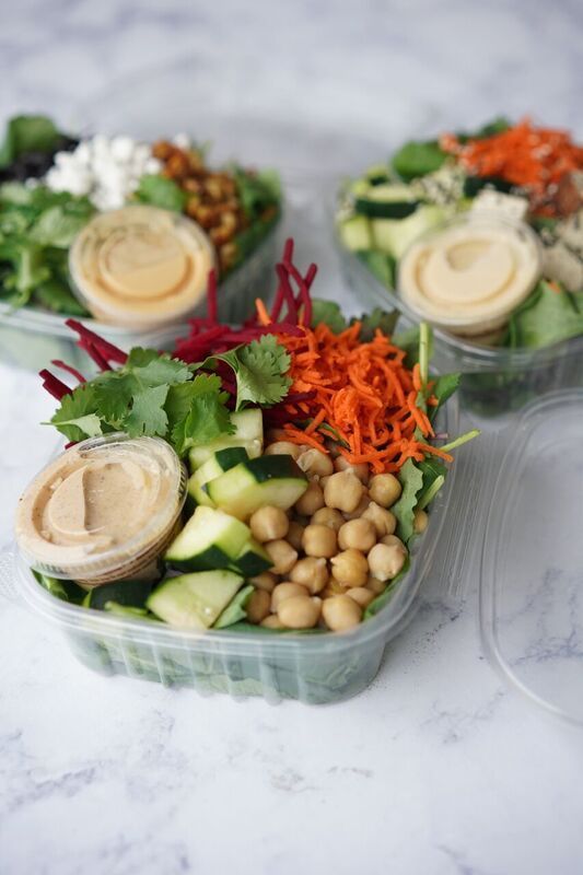 Fresh salad meal prep bowls with chickpeas, cucumbers, shredded carrots, greens, and hummus cups