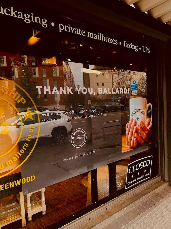 Storefront window sign reading “Thank You, Ballard” with “Closed” notice at night