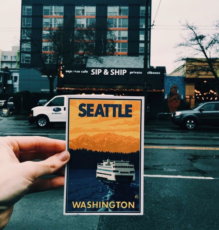 Hand holding a Seattle, Washington postcard with a ferry; street and building in the background