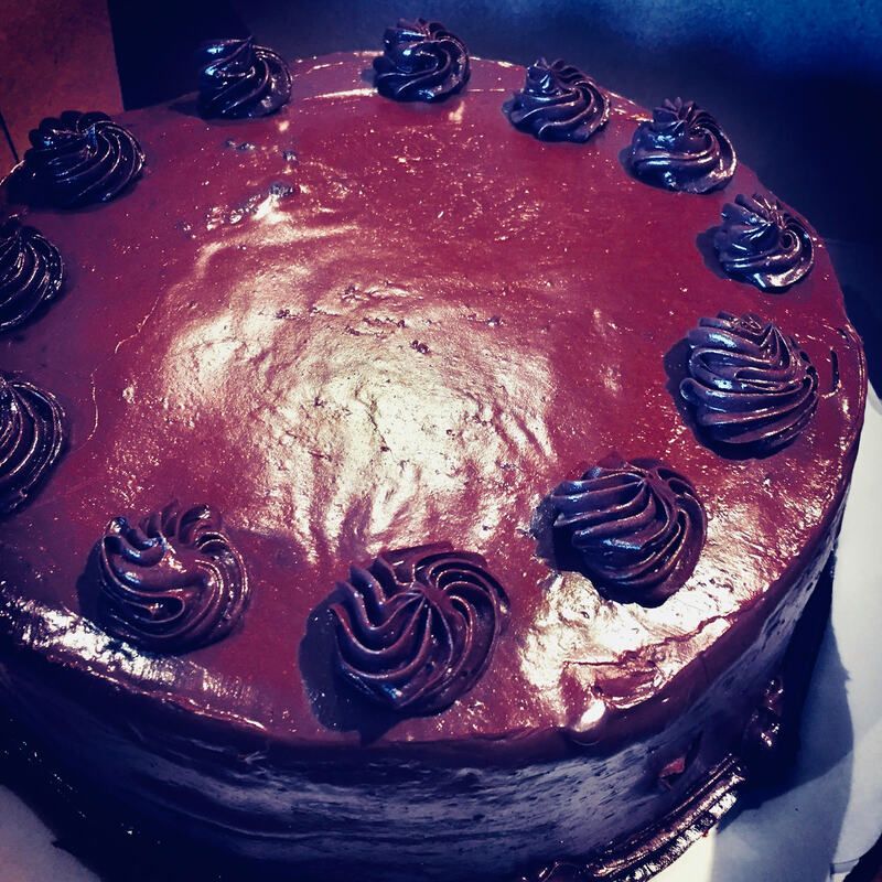Chocolate cake with glossy burgundy frosting and decorative piped swirls on top.