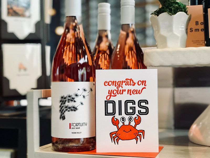 Wine bottles and a “Congrats on your new DIGS” card with a crab on a shelf