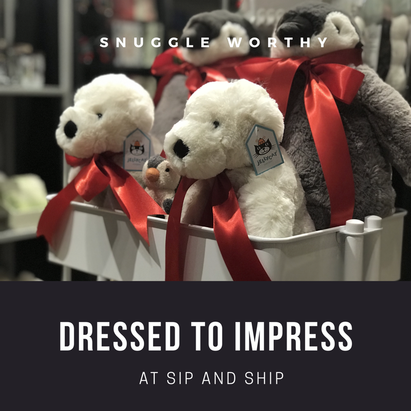 White plush dogs with red ribbon bows in a store display; text reads “Snuggle Worthy” and “Dressed to Impress.”