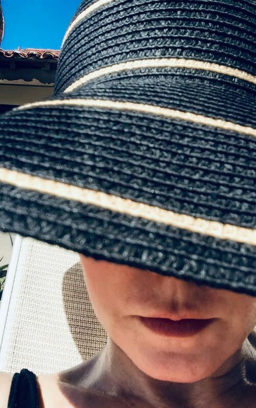 Person wearing a wide-brimmed striped hat, face mostly covered by the brim, outdoors in bright sunlight