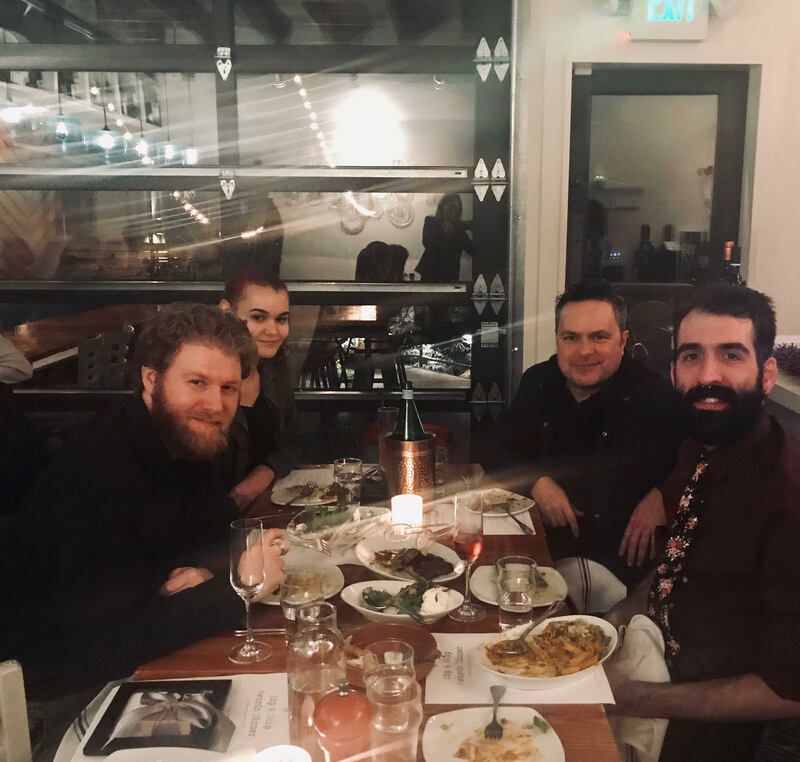 Four people seated at a restaurant table with plates, glasses, and a lit candle centerpiece