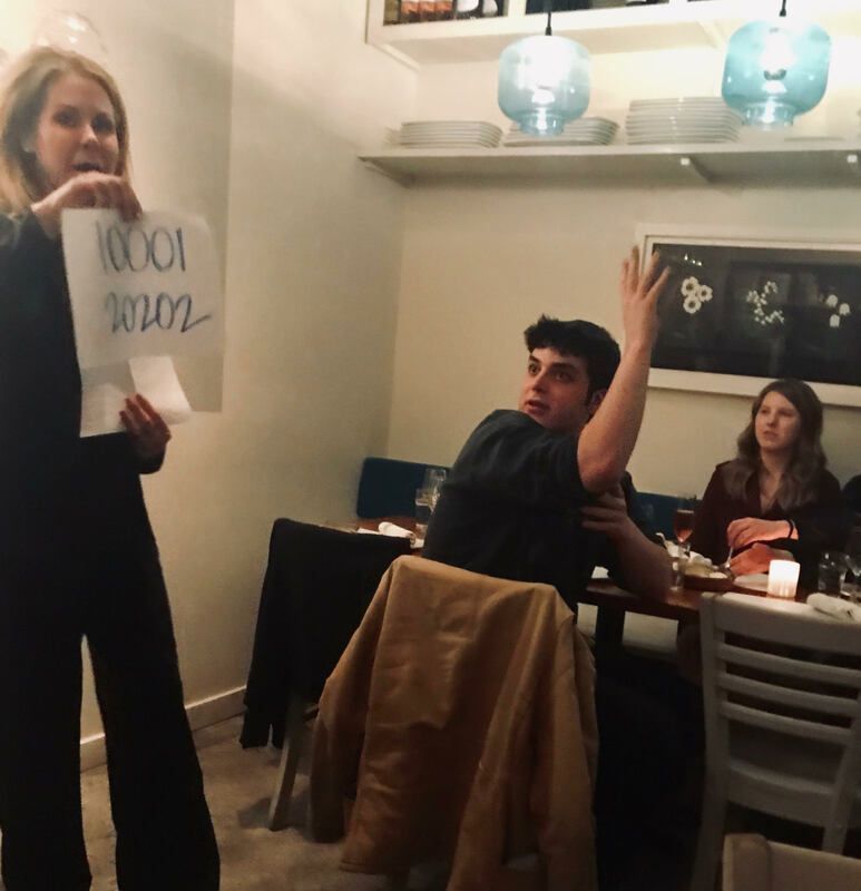 Person holds up a sign while others sit at a dining table in a warmly lit room.