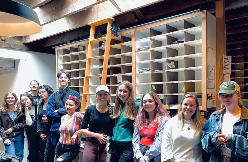 Group of people standing indoors in front of tall wooden shelves, smiling and posing for a photo.
