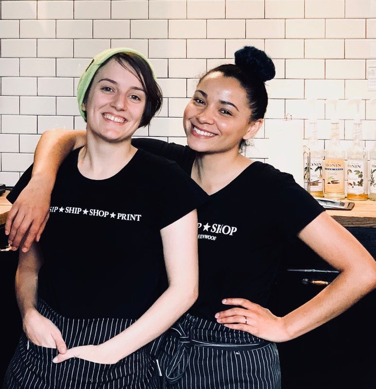 Two smiling café staff in black shirts and striped aprons standing behind a counter