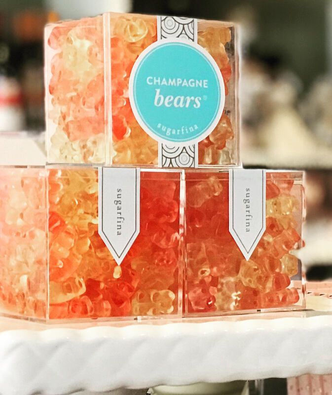 Stacked orange champagne bears in clear gift boxes with teal labels on a white cake stand