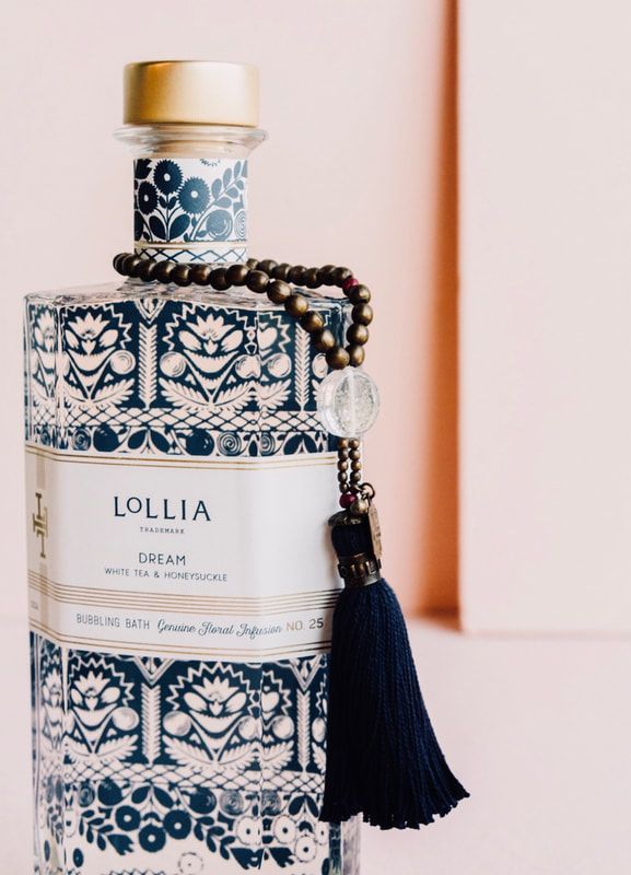 Decorative blue-and-white Lollia perfume bottle with a tassel on a light pink background