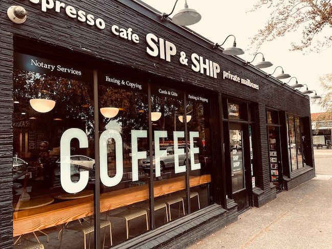 Coffee shop storefront with large “COFFEE” window lettering and “SIP & SHIP” sign on a rainy street