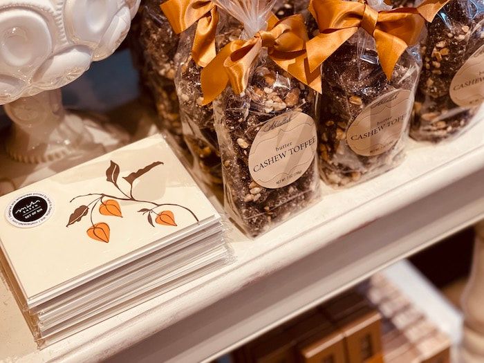 Gift display with card packets and clear treat bags tied with orange ribbons on a white shelf