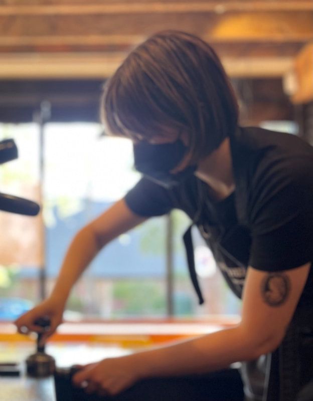 Masked person stirring a pot in a kitchen near a bright window