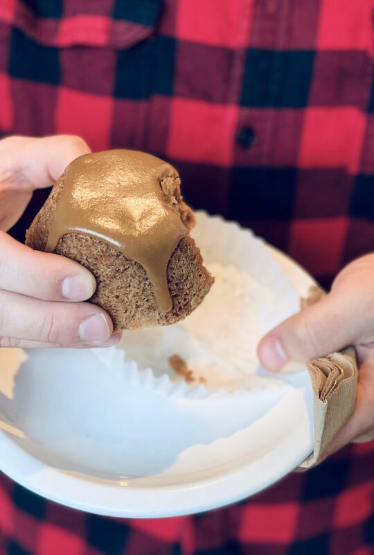 Hands holding a chocolate-frosted cupcake over a white plate, with a red-and-black plaid shirt in the background