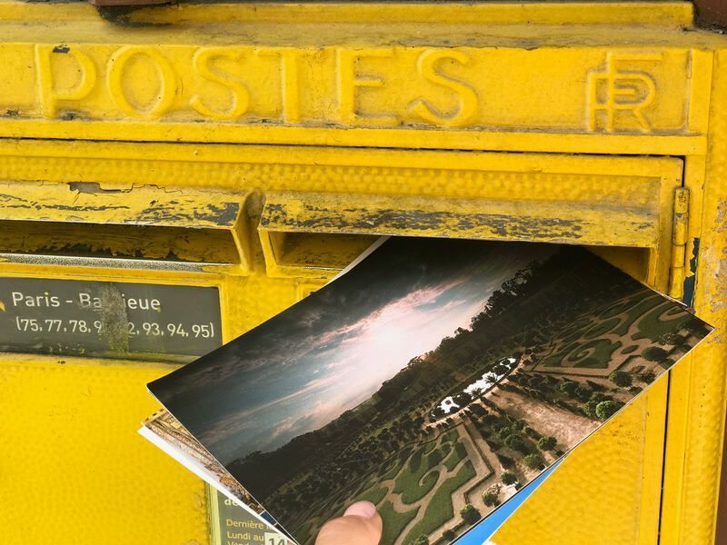Poste yellow mailbox with postcards sticking out, including a scenic aerial landscape photo