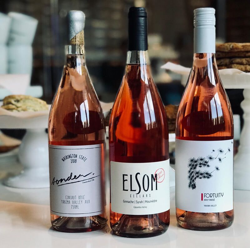 Three rosé wine bottles on a table, with black, white, and silver caps and labels.