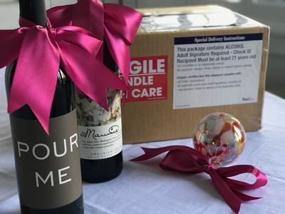 Magenta gift box with ribbon, Pour Me bottle bag, wine bottle, and small decorative ornament