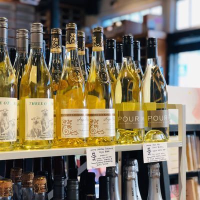 Bottles of white wine displayed on a store shelf with price tags, in a bright shop interior