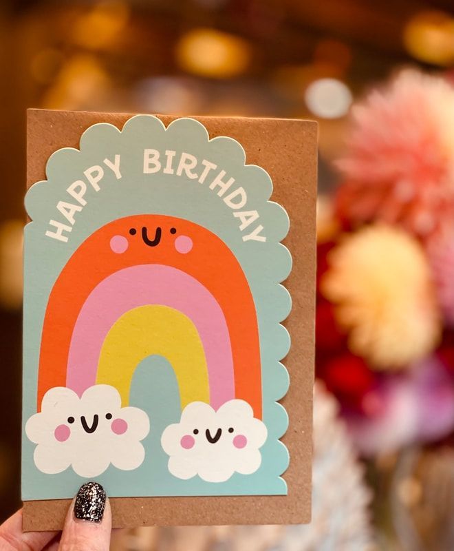 “Happy Birthday” card with a colorful rainbow and smiling cloud flowers on a brown background