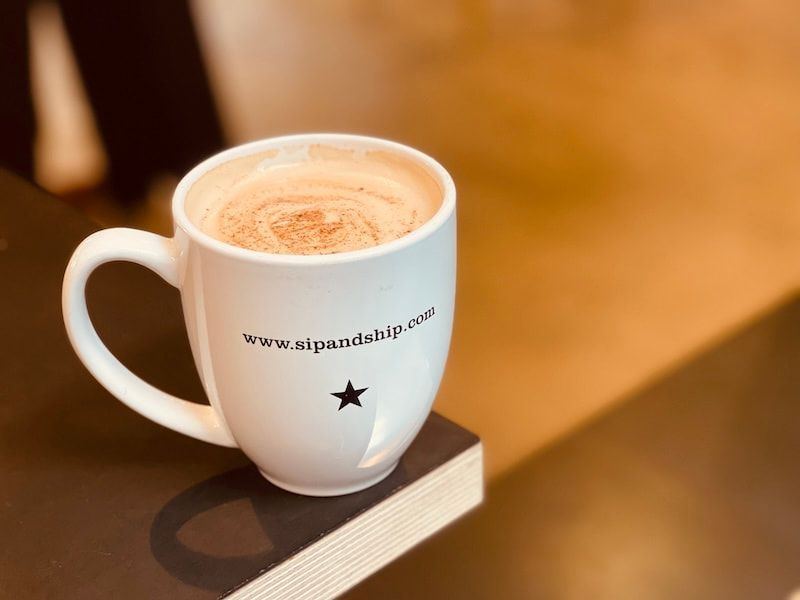 White coffee mug with latte on a wooden table, showing a website URL and star logo