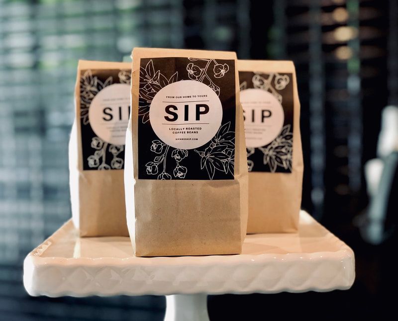 Three small beige SIP treat bags on a white tray, with black floral labels, on a table.