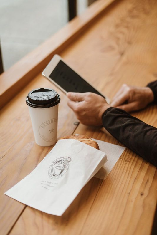 Person using a tablet at a wooden café table beside a coffee cup and a sketchbook