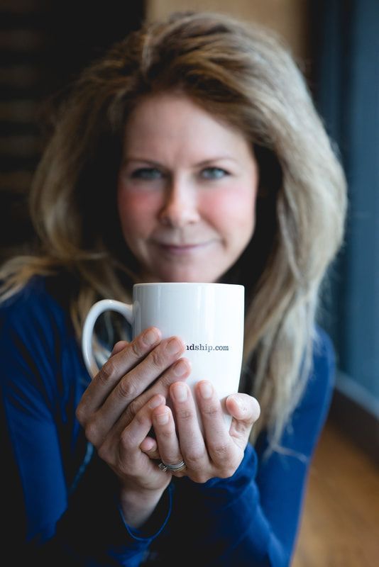 Woman in a blue sweater holding a white mug and smiling in a softly lit indoor setting