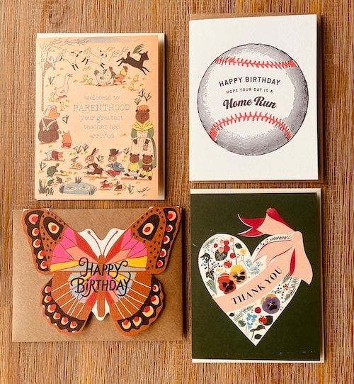 Four handmade birthday cards on a wooden surface, including a baseball card and a butterfly card.