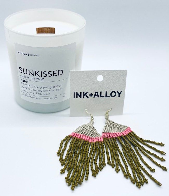 White candle jar and green beaded earrings on display card labeled INK+ALLOY