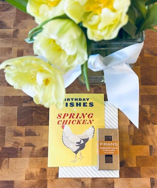Yellow tulips over a yellow book and chocolate bar on a wooden table with a white ribbon