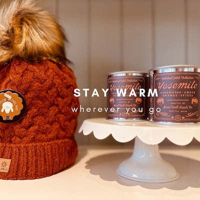 Cozy knit hat beside two warm drink cans on a small white pedestal, with text “STAY WARM wherever you go”